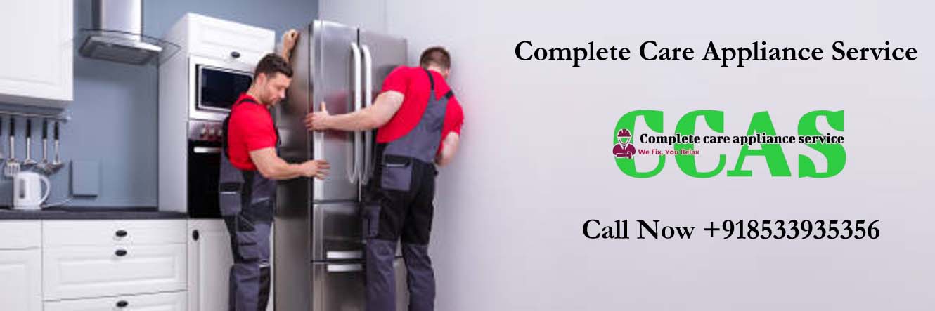 Two Young Male Movers In Uniform Placing Modern Steel Refrigerator In Kitchen