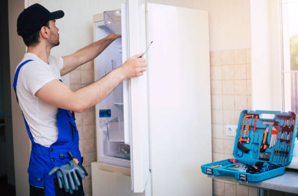 Professional young repairman in worker uniform and cap with modern toolbox with equipment is repairing of refrigerator on the kitchen