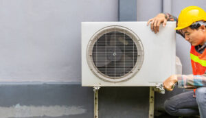 The air conditioner technician Uses a wrench to tighten the nut of the air compressor. Young Asian man repairman checking an outside air conditioner unit.