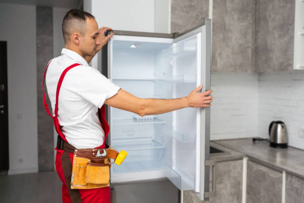 Happy adult handyman repairing refrigerator in domestic kitchen. High quality photo